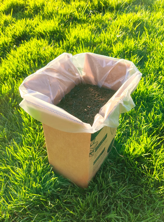 Caja abierta de Compostcat mostrando textura terrosa en pasto